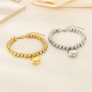 Dettaglio di bracciali a sfere in oro e argento con ciondoli a cuore su seta