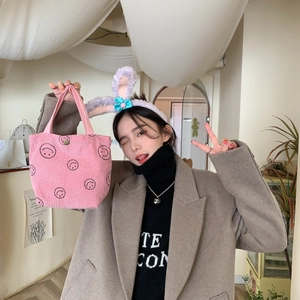 Detailed texture of pink corduroy handbag with black smiley face pattern in a lifestyle setting
