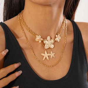 Layered gold necklace featuring metallic starfish and flower pendants on figaro chains