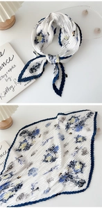 Detail of pleated silk scarf featuring blue floral patterns and white base with blue border
