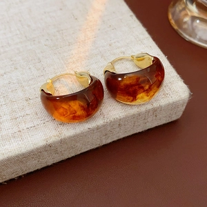Macro view of amber resin hoop earrings with gold-plated metal clasp on linen texture