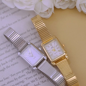 Detail view of silver and gold square quartz watches on a book with white flowers