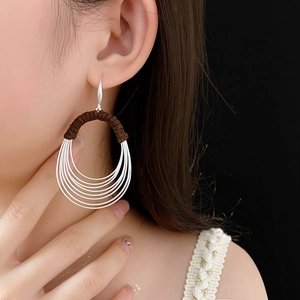 Detail of silver multilayer oval hoop earrings with brown wrap accent on a model