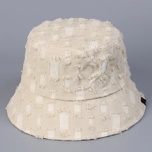Détail d'un chapeau bob en toile crème avec trous effilochés et étiquette de marque