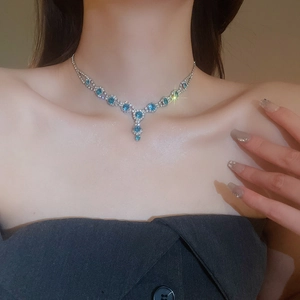 Close-up of a silver necklace featuring an elegant blue gemstone flower pendant on model