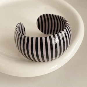 Detail of a wide C-shaped open bangle with black and white vertical stripes on a white tray