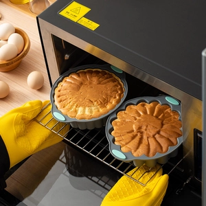 Gray sunflower silicone cake molds with blue handles being removed from a hot oven