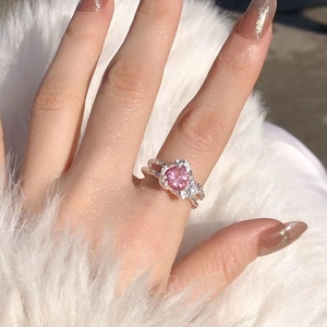 Close-up of sparkling pink heart-shaped zircon ring on finger with soft white background