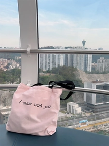 Detail of light pink canvas tote bag with black letter print and sturdy black shoulder straps