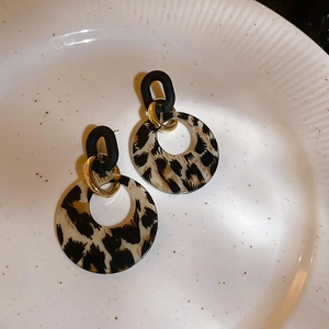 Close-up of retro leopard print acrylic earrings with black matte hoops and gold metal links
