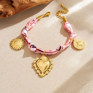 Bracelet en tissu rose avec pendentifs cœur et soleil dorés sur fond beige