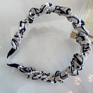 Twisted paisley print headband with white pearls on a minimalist marble background