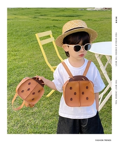 Detail shot of orange ladybug backpack on toddler in a grassy outdoor playground setting