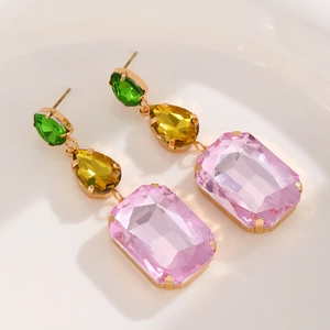 Macro detail of tricolor geometric crystal drop earrings with faceted stones and gold finish