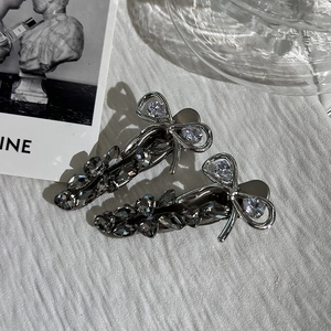 Detailed close-up of two silver bow hair clips with grey crystals and floral motifs