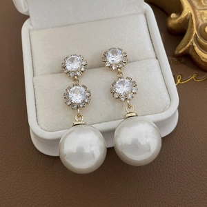Vue détaillée de boucles d'oreilles dorées avec strass et perles blanches en coffret