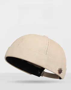 Detail view of beige docker cap featuring a metallic maple leaf charm on canvas fabric