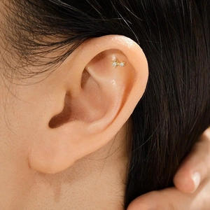 Detailed view of a gold star stud earring with inlaid gems worn on the ear cartilage