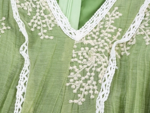 Detail of green V-neck dress with intricate white floral embroidery and lace trim