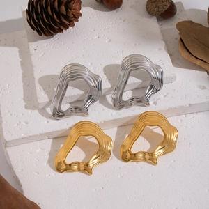 Irregular fluid-shaped gold and silver earrings on stone with natural autumn decor
