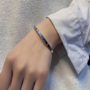 Close-up of minimalist silver stainless steel open bangle worn with a white shirt