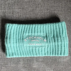 Detailaufnahme des blaugrünen Strickstirnbands mit weißem Stockholm-Sweden-Schriftzug