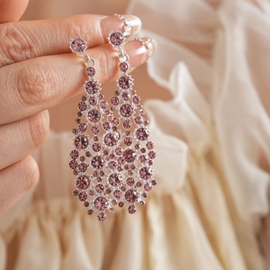 Detalle de pendientes largos de gota en metal plateado y pedrería púrpura sujetos en mano