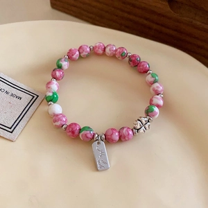 Detail of colorful floral beaded bracelet with silver clover charm in a ceramic dish