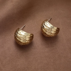 Detailed close-up of C-shaped golden earrings with textured hammered metal finish