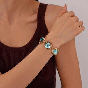 Close-up of vintage gold bracelet with blue resin stones and leaf carvings on a wrist
