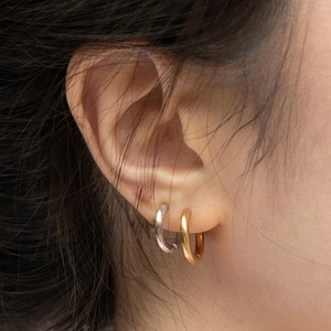 Minimalist silver and gold geometric hoop earrings shown on ear with a polished metal finish