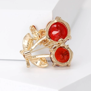 Elegant gold cherry brooch featuring faceted red crystals and polished metal leaves