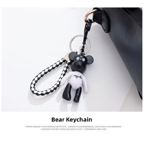 Detail view of a black and white bear keychain with a checkered strap on a handbag