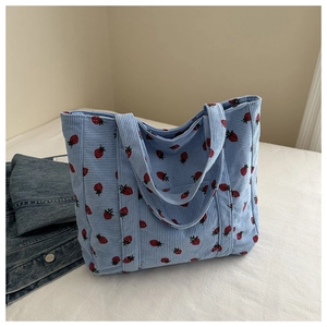 Detail of light blue corduroy tote bag featuring red strawberry patterns and soft texture