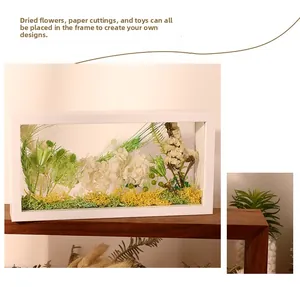 White rectangular shadow box frame with dried flowers and green moss display on wood shelf