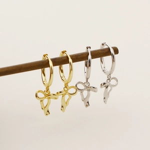 Close-up of gold and silver bow-knot ribbon earrings hanging on a minimalist wood stand