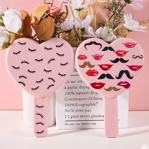 Pink heart-shaped handheld makeup mirrors with eyelash and lip patterns on white surface
