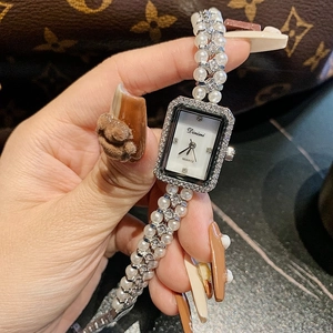 Close-up of elegant square dial watch with pearl bracelet and diamond bezel