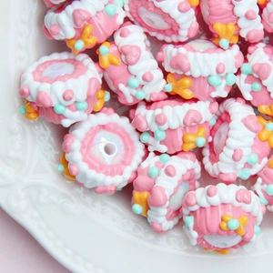 Close-up of pink hand-painted candy beads with cream details in a white ceramic bowl