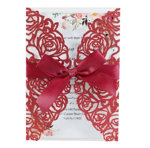 Detail of red glitter laser-cut rose wedding invitation with a satin ribbon bow and insert