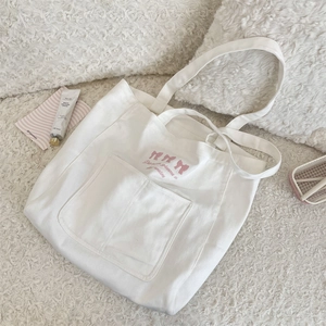 Gros plan du sac cabas en toile blanche avec broderie nœud rose et grande poche avant