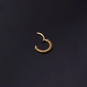 Macro d'un anneau de piercing doré à charnière avec une texture spirale sur fond noir