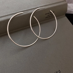 Macro detail of large silver geometric C-shaped earrings on a textured book surface