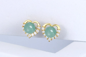 Macro shot of heart-shaped gold earrings featuring green gemstones and white zircon halo