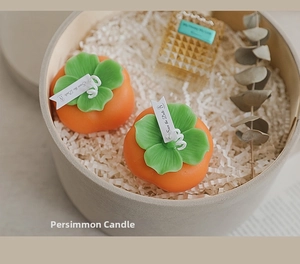 Close-up of lifelike orange persimmon candles in a round gift box with eucalyptus leaves