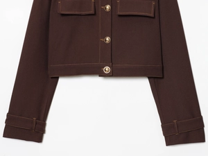 Close-up of brown short jacket showing golden embossed buttons and yellow contrast stitching