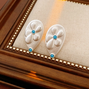 Close-up of vintage silver teardrop earrings with floral relief and turquoise stones