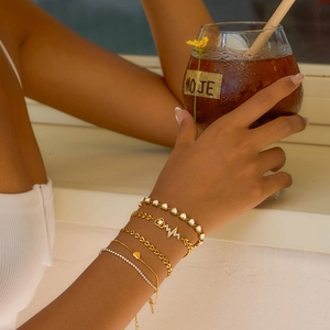 Detail showing stacked gold stainless steel bracelets with heart and zircon accents on wrist