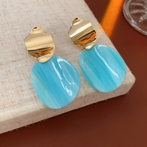 Gros plan de boucles d'oreilles en acrylique bleu irrégulier et métal doré texturé