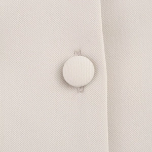 Detalle de un botón forrado en tela en un vestido de popelina beige claro tejido